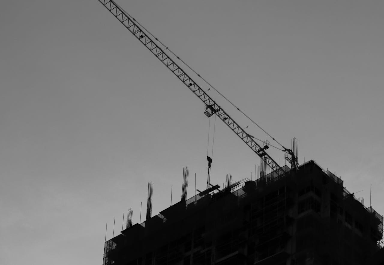 A silhouette of a construction crane and building under construction at sunset.