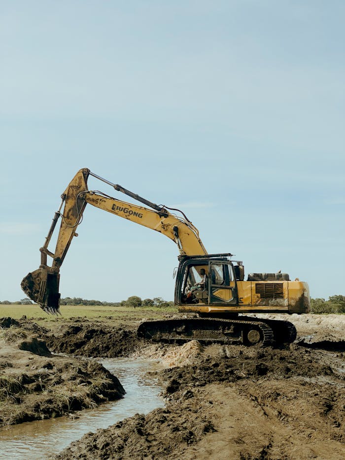 Excavator operating in a muddy field, showcasing industrial construction machinery during a sunny day.