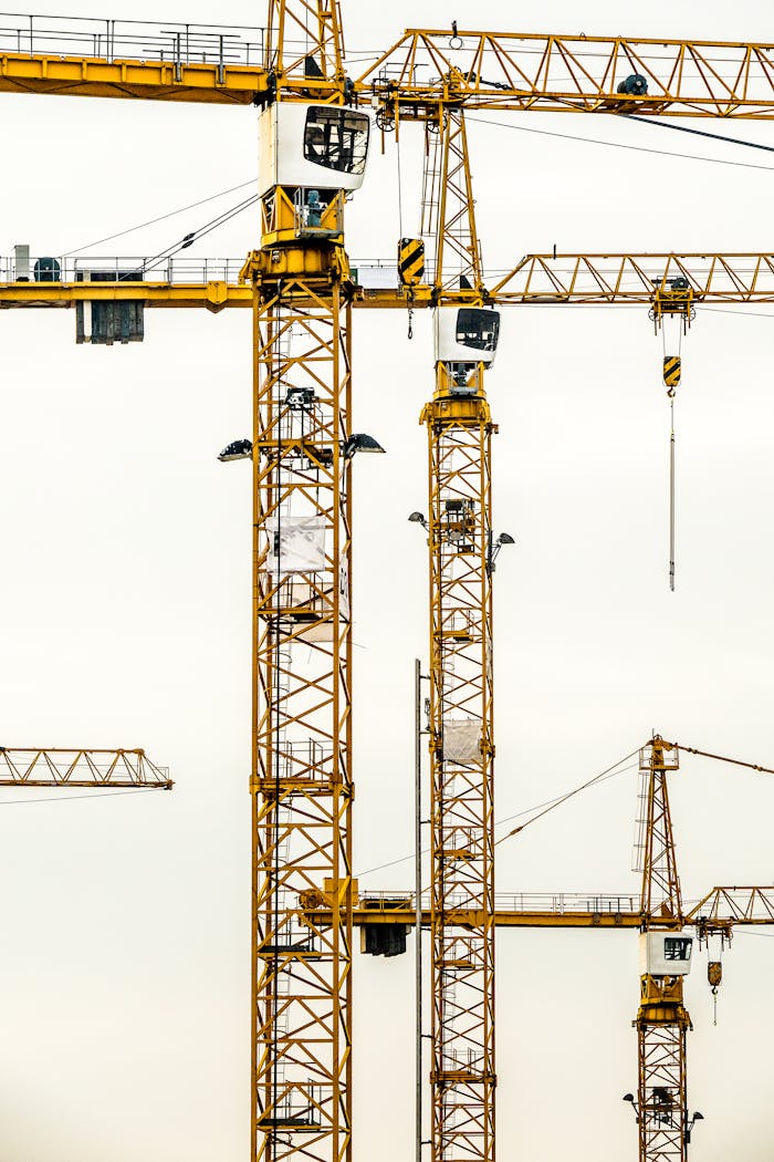 Vertical shot of multiple construction cranes towering against a cloudy sky.