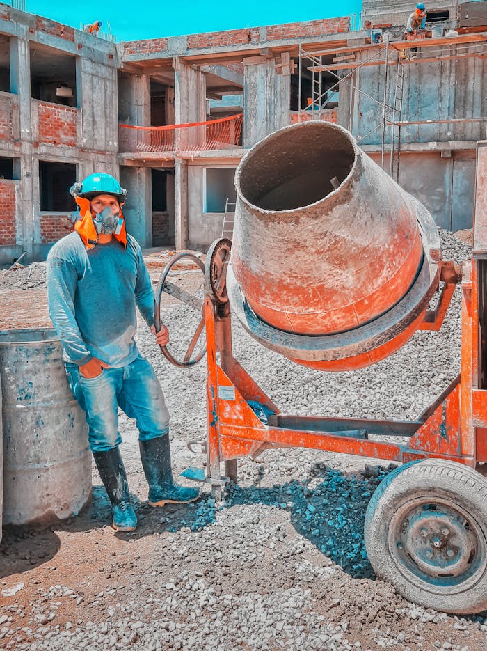 Construction worker operates heavy concrete mixer on sunny outdoor site.