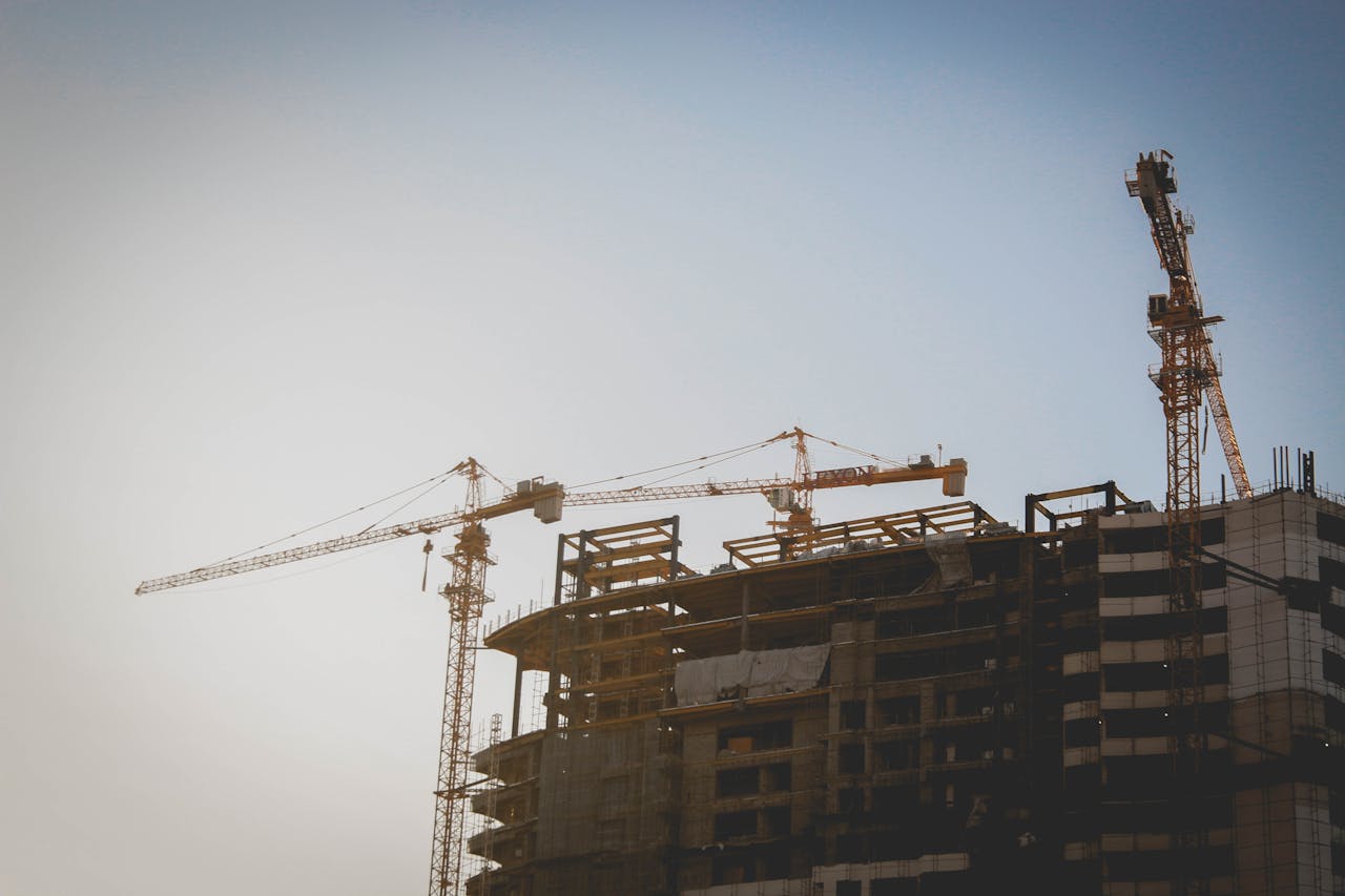 A high-rise building under construction with tower cranes against a clear sky.